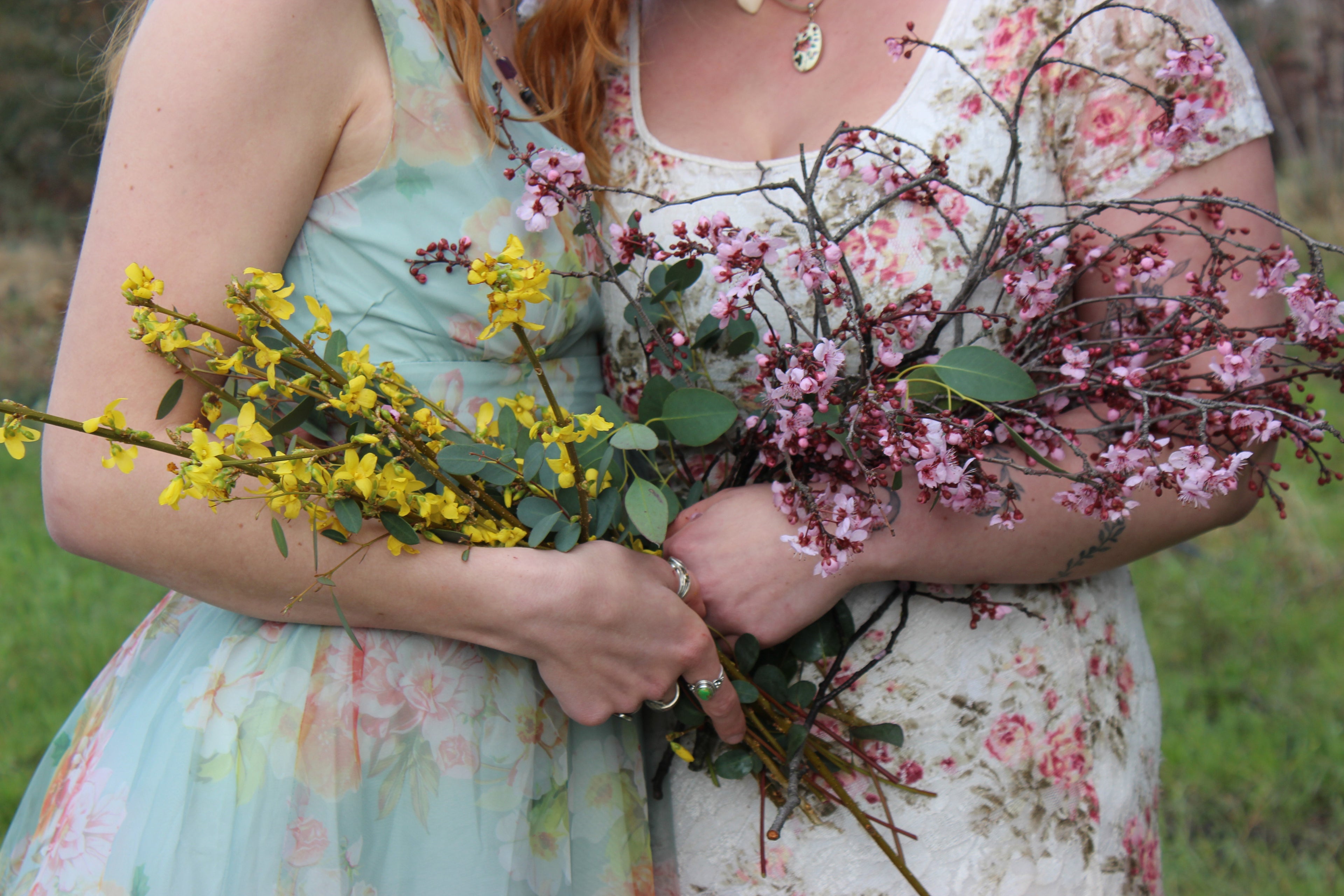 Two women holding a bouquet of flowers outdoors.